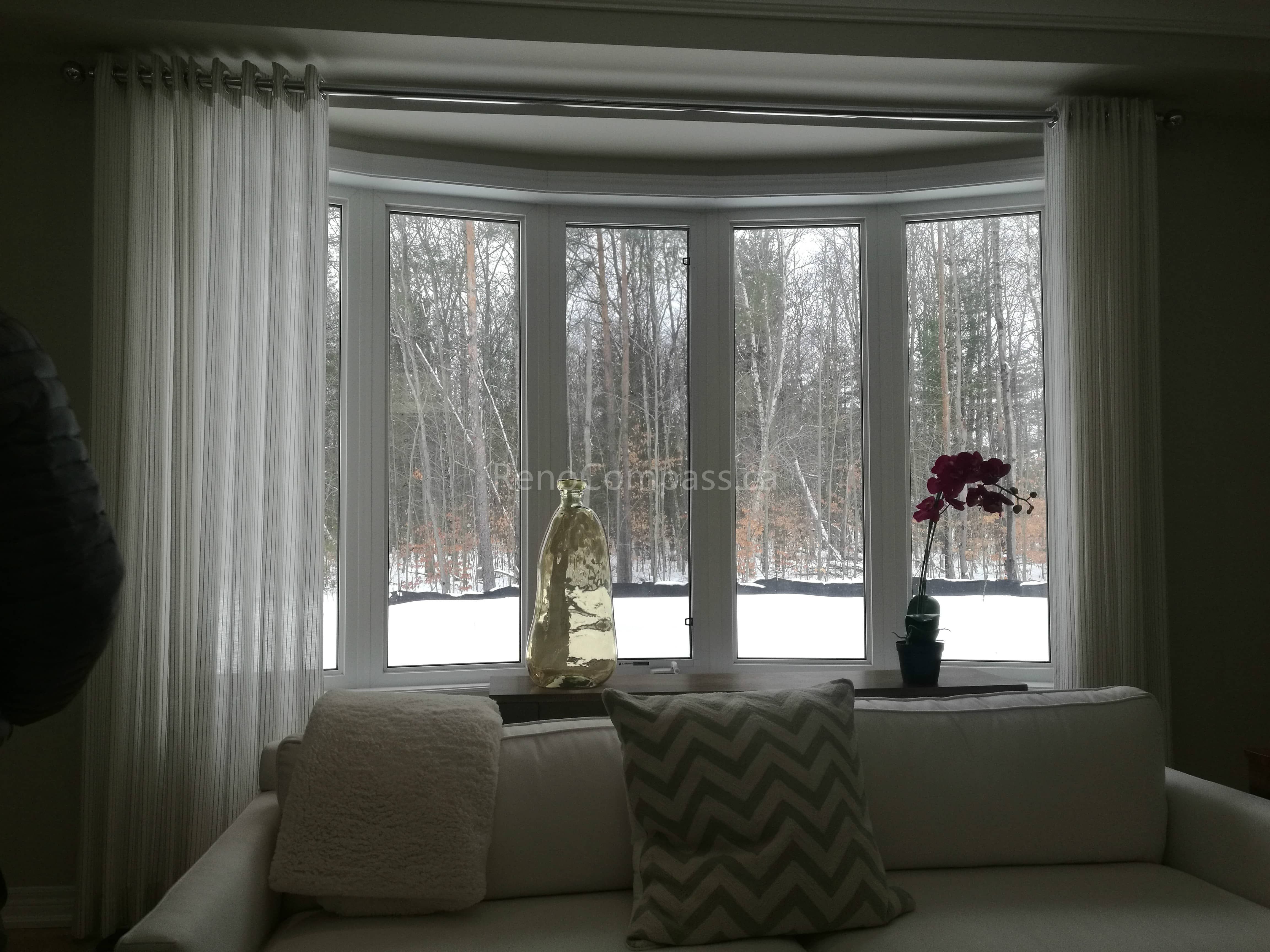 This image showcases a beautifully finished living room as part of a Toronto interior renovation project. The curved bay window design allows abundant natural light to flow into the space, creating a calm and inviting atmosphere. Soft white curtains, clean window framing, and a neutral sofa setup enhance the overall brightness and comfort of the room. The renovation emphasizes natural views, elegant proportions, and a timeless interior aesthetic, reflecting high-quality interior renovation craftsmanship in Toronto homes.