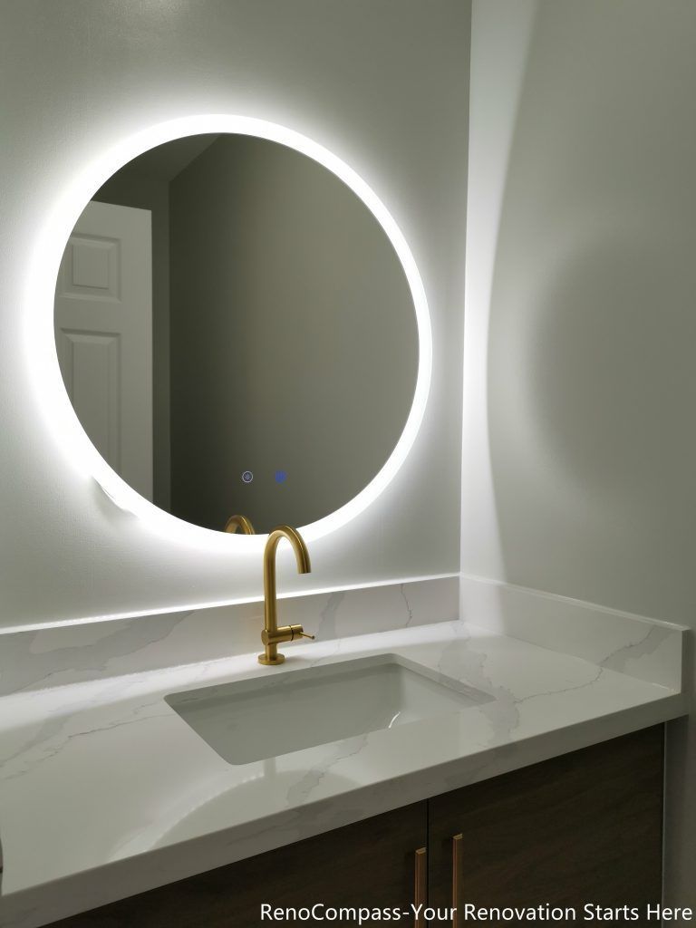 This Oakville bathroom renovation features a modern vanity design with a quartz countertop, undermount sink, and elegant gold faucet paired with a round LED backlit mirror. The soft lighting enhances brightness while creating a clean and contemporary atmosphere. Custom wood cabinetry provides functional storage while maintaining a sleek modern aesthetic. Completed by a professional Toronto renovation company, this bathroom upgrade combines style, practicality, and high-quality finishes to create a refined and comfortable everyday space.