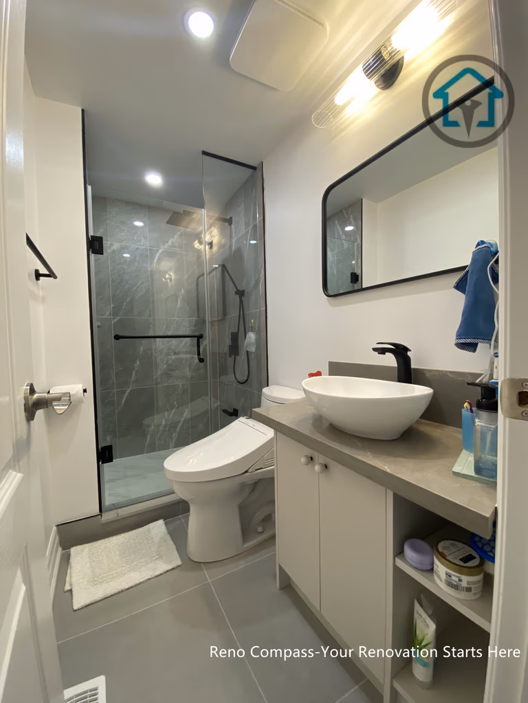 This compact bathroom renovation in Toronto demonstrates how thoughtful layout planning can maximize both comfort and functionality in a limited footprint. The design features a frameless glass shower enclosure with large-format wall tiles, creating a visually open and seamless look. A floating-style vanity with integrated storage, vessel sink, and matte black fixtures adds a modern touch while maintaining practicality. Neutral finishes, recessed lighting, and clean sightlines help the space feel bright, efficient, and well-balanced for everyday use.