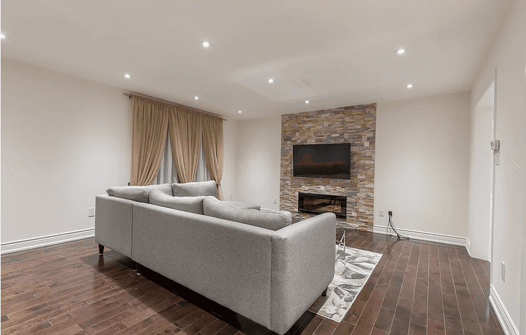 A welcoming modern living room from our Vaughan full house renovation featuring a stone fireplace wall, mounted TV, and elegant neutral décor. The comfortable sectional sofa and hardwood flooring create a perfect balance of style and warmth for everyday family living.