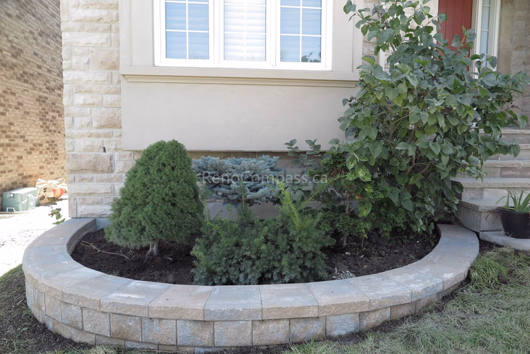 This Markham landscaping upgrade features a custom-built curved garden bed with a natural stone retaining wall, designed to enhance the home’s front yard curb appeal. The raised planter structure defines the entrance area while providing proper soil support and drainage for shrubs and seasonal greenery. Blending soft landscaping with durable hardscape construction, this front yard improvement delivers a clean, welcoming appearance. Completed by a professional Toronto renovation company, the project adds both visual charm and long-term landscape functionality.