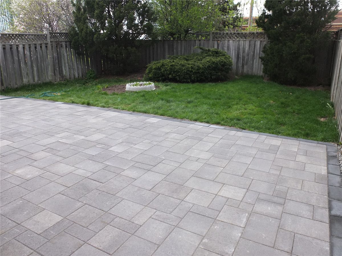 A completed backyard interlocking patio installation in Mississauga featuring large-format grey stone pavers, clean edge borders, and a modern low-maintenance outdoor design. This landscaping renovation improves outdoor usability and creates a durable patio space ideal for relaxation and gatherings. Completed by a professional Toronto Renovation Company, Reno Compass Inc., specializing in interlocking, landscaping, and exterior home upgrades across the GTA.