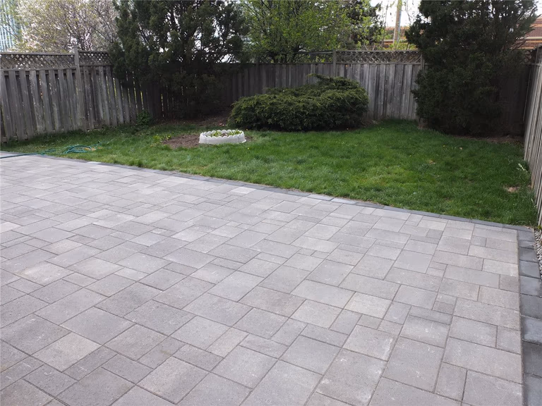 A completed backyard interlocking patio installation in Mississauga featuring large-format grey stone pavers, clean edge borders, and a modern low-maintenance outdoor design. This landscaping renovation improves outdoor usability and creates a durable patio space ideal for relaxation and gatherings. Completed by a professional Toronto Renovation Company, Reno Compass Inc., specializing in interlocking, landscaping, and exterior home upgrades across the GTA.