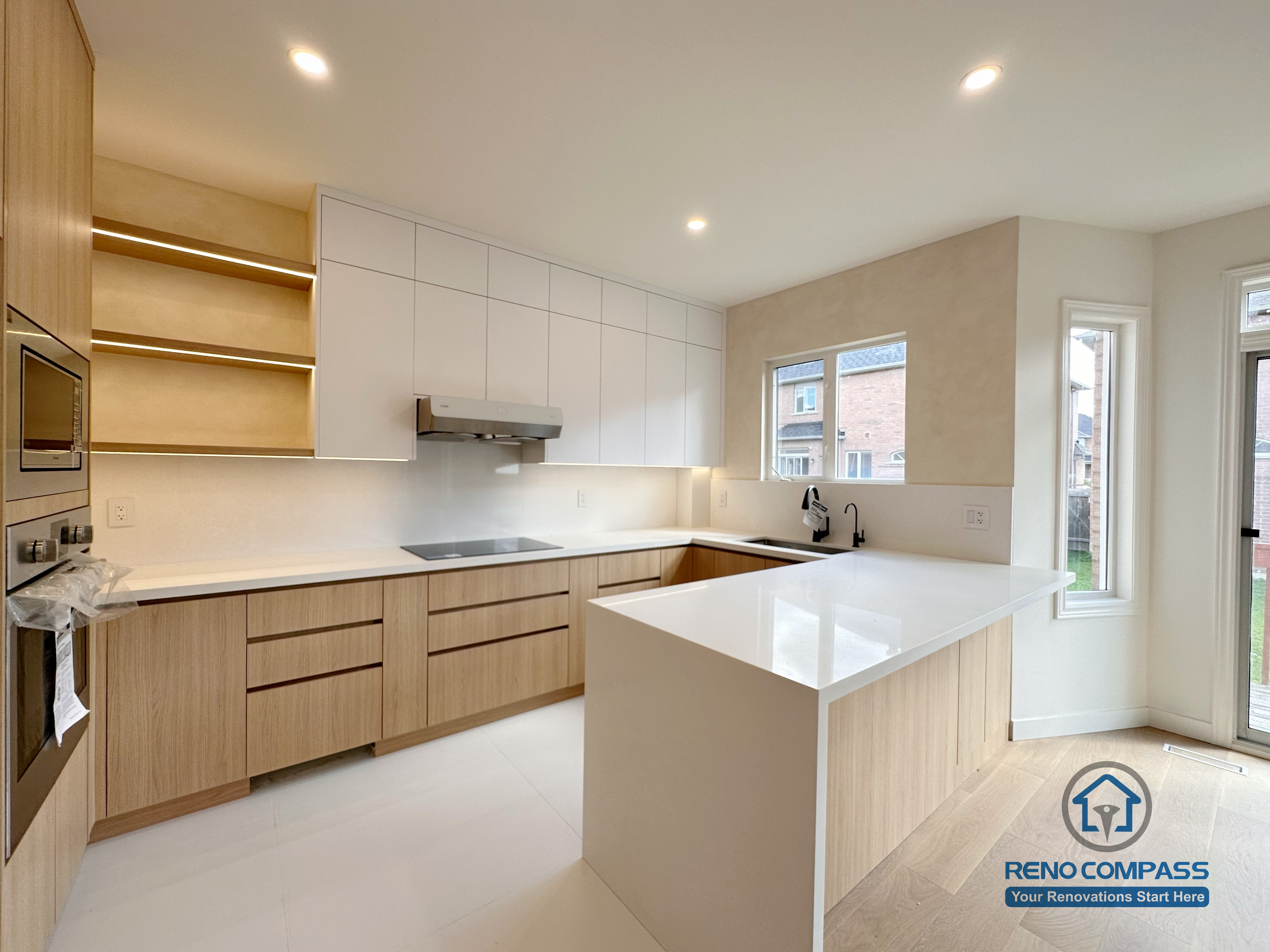 Modern kitchen renovation in Markham featuring custom wood cabinetry, a large waterfall island, integrated appliances, and clean white finishes. The open-concept layout maximizes natural light, improves workflow, and creates a functional yet refined kitchen space for daily living.