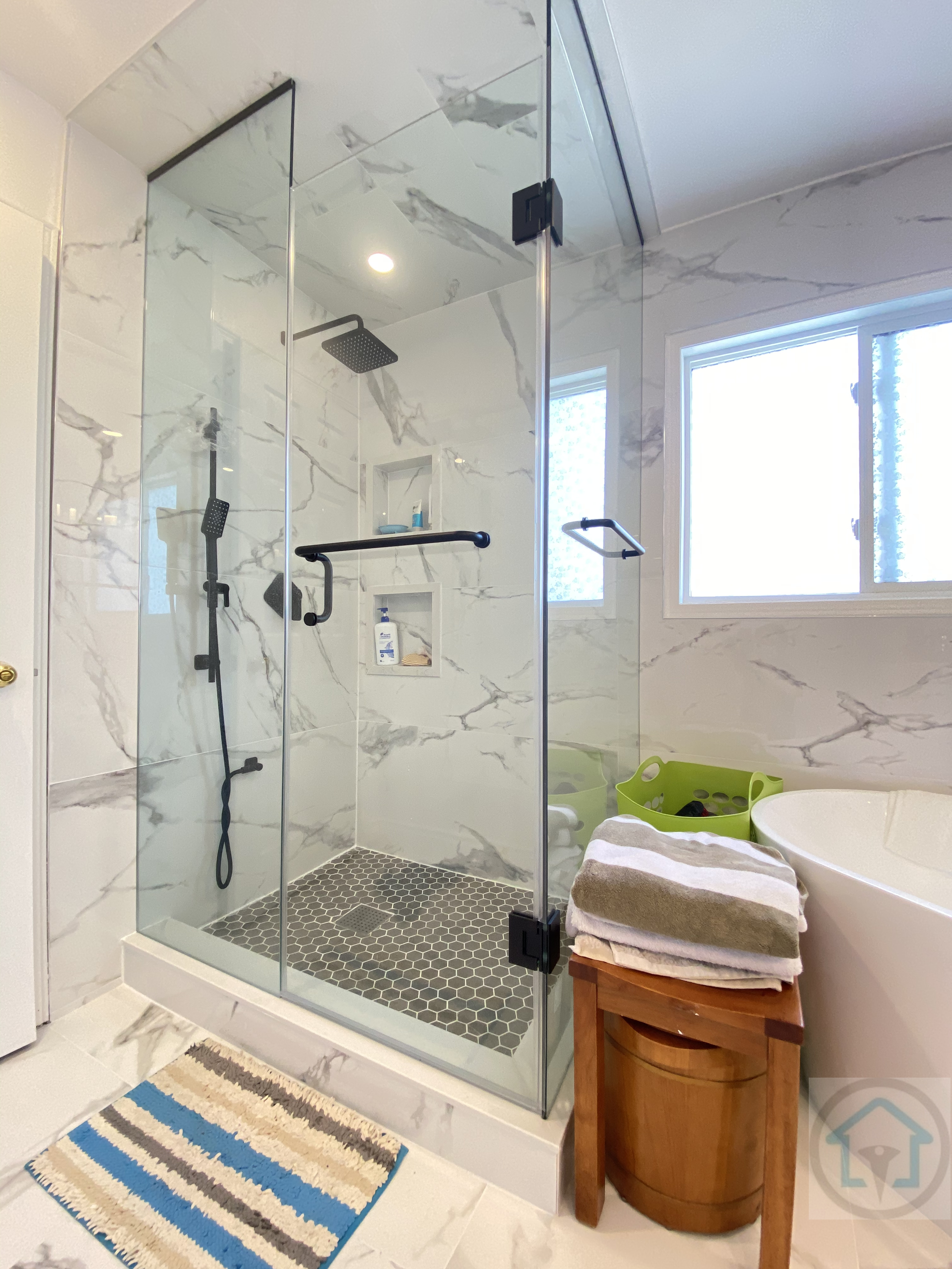 This Richmond Hill bathroom renovation highlights a custom glass-enclosed shower with marble-look wall tiles and a dark mosaic shower floor for added slip resistance. Black shower fixtures and hardware create a modern contrast against the light stone finishes, while the frameless glass design enhances openness and natural light. Completed by Reno Compass Inc., this bathroom remodel balances safety, functionality, and clean contemporary design for Richmond Hill homes.