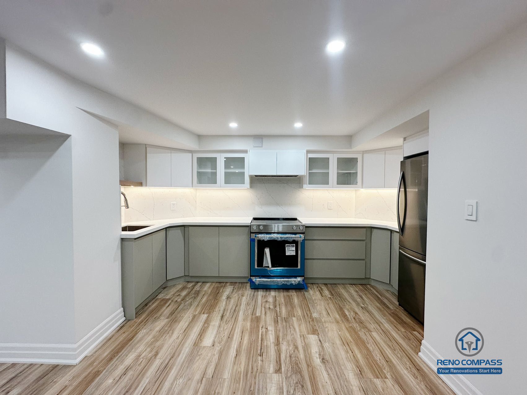 This image shows a completed basement kitchen renovation in Pickering, captured from a front-facing perspective to highlight the symmetrical layout and clean cabinet alignment. Custom cabinetry, integrated under-cabinet lighting, and a continuous countertop surface create a functional and visually balanced workspace. Neutral tones and consistent flooring help the kitchen blend seamlessly into the surrounding basement living area, supporting everyday use without visual clutter. Recessed ceiling lighting enhances brightness and clarity, reinforcing a practical, well-organized lower-level kitchen design.