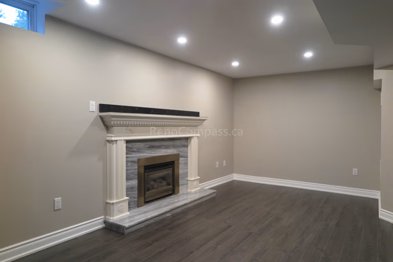 This Markham basement renovation features a beautifully finished living space with a classic decorative fireplace mantel, recessed LED pot lights, and durable dark wood flooring. The neutral wall tones and clean trim details create a warm and inviting atmosphere perfect for a family lounge, entertainment area, or secondary living space. Completed by Reno Compass, a trusted renovation contractor specializing in basement finishing and full interior renovations across Markham and the Greater Toronto Area.