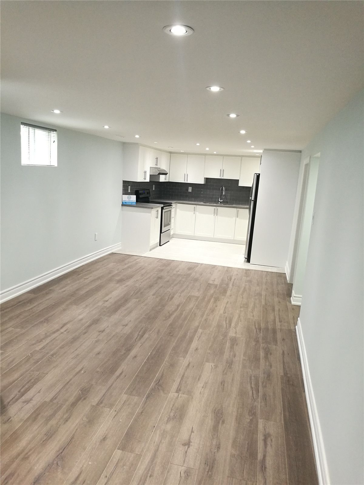 Open-concept basement interior renovation in Pickering featuring continuous wood-look flooring, recessed pot lighting, and a modern white kitchen with dark tile backsplash. This bright and functional layout maximizes usable living space and demonstrates the quality craftsmanship of a professional Toronto renovation company.