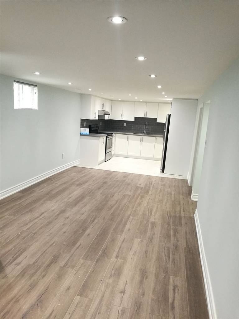 Open-concept basement interior renovation in Pickering featuring continuous wood-look flooring, recessed pot lighting, and a modern white kitchen with dark tile backsplash. This bright and functional layout maximizes usable living space and demonstrates the quality craftsmanship of a professional Toronto renovation company.