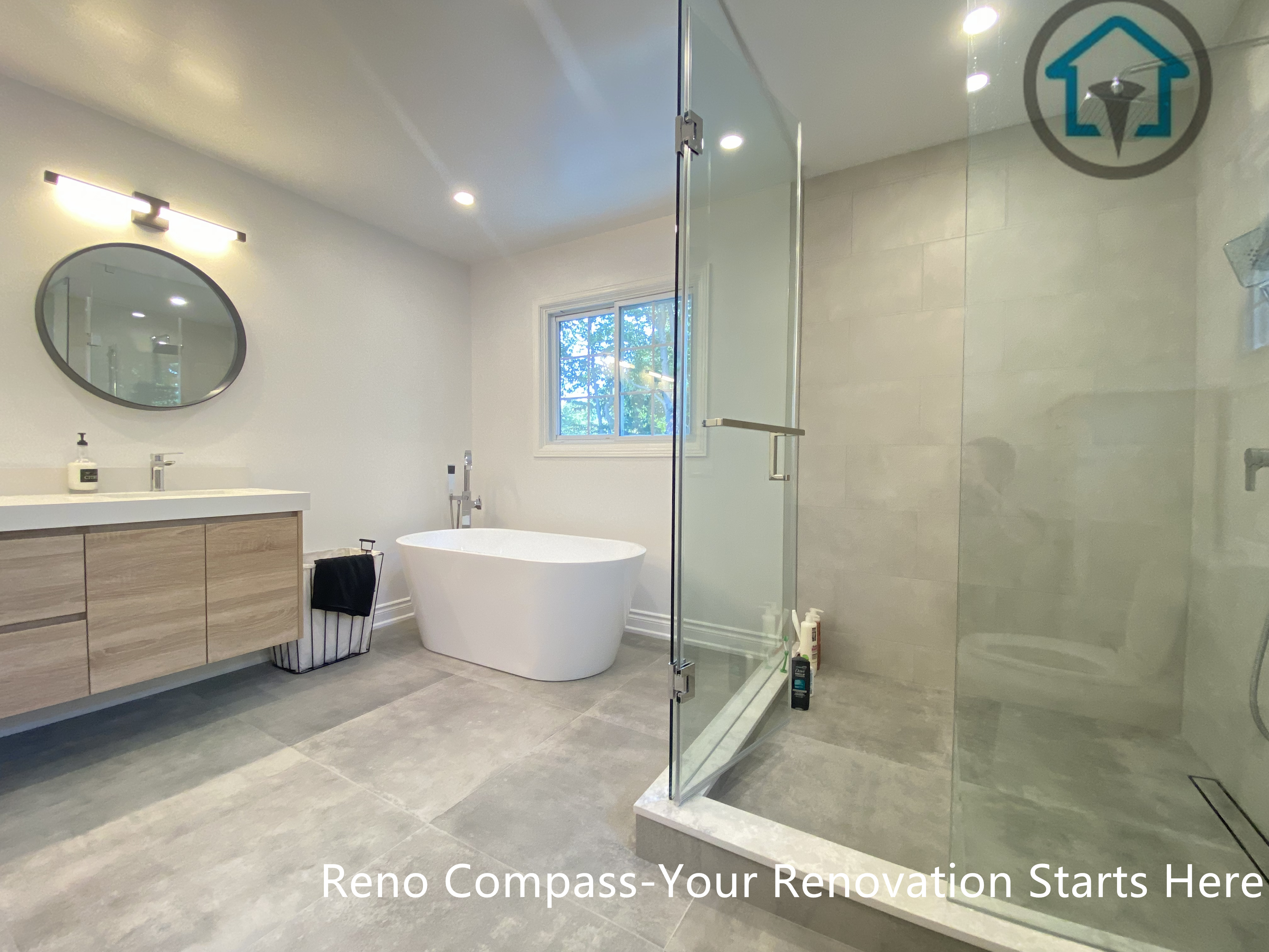 This Oakville bathroom renovation features a clean, modern layout with a freestanding bathtub and a frameless glass shower enclosure. Large-format neutral tiles create a seamless, spa-like atmosphere, while the floating wood vanity and round mirror add warmth and balance. Designed for comfort and long-term usability, this bathroom combines natural light, open circulation, and timeless finishes to elevate everyday living.
