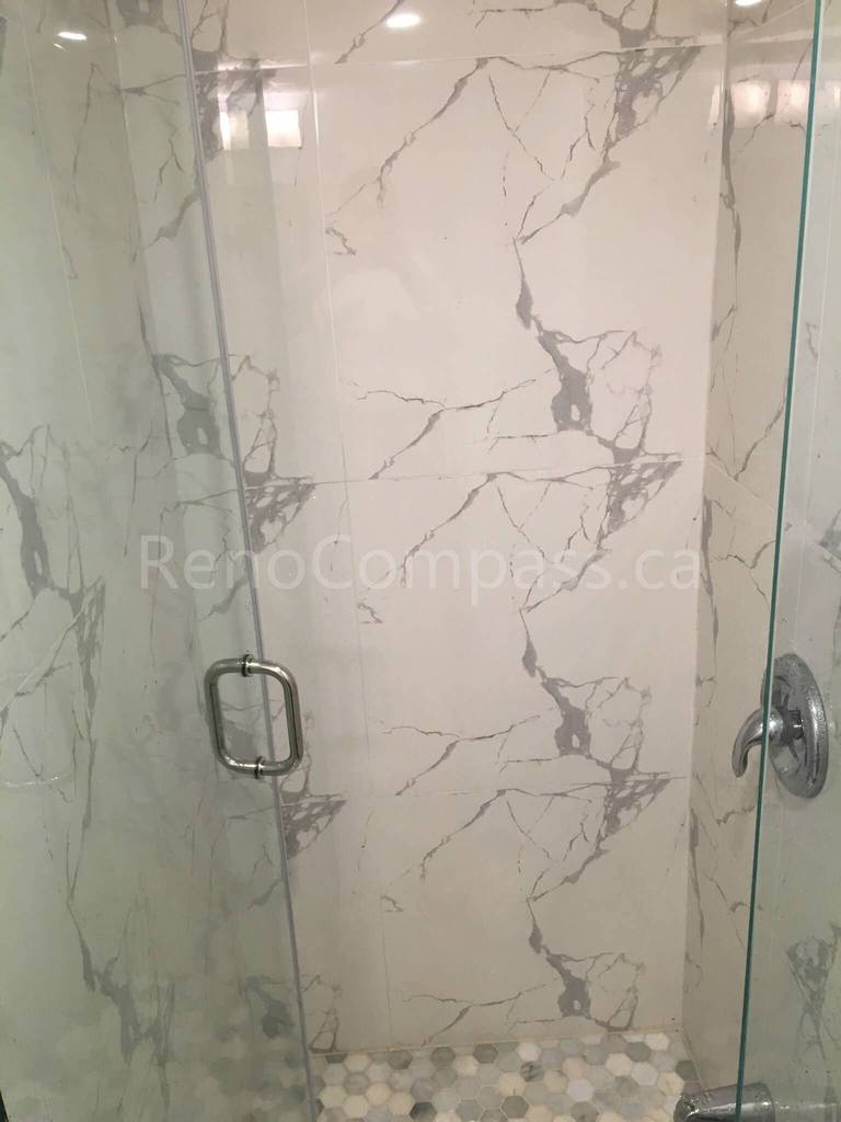A luxurious frameless glass shower enclosure featuring elegant marble-pattern wall tiles and pebble-style flooring. This Mississauga bathroom renovation by Reno Compass delivers a spa-like experience with high-end materials and craftsmanship.