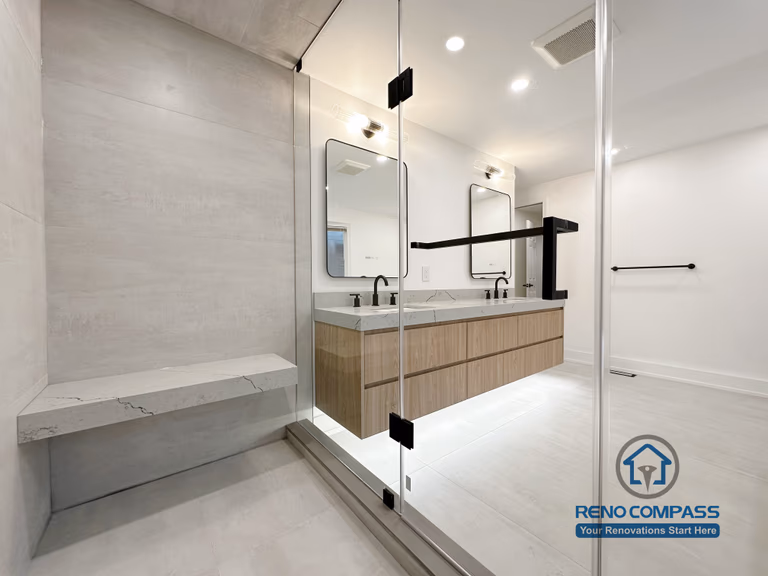 Modern bathroom renovation in Oakville featuring a frameless glass shower, built-in shower bench, and custom double vanity with quartz countertop, completed by a professional Toronto renovation company.