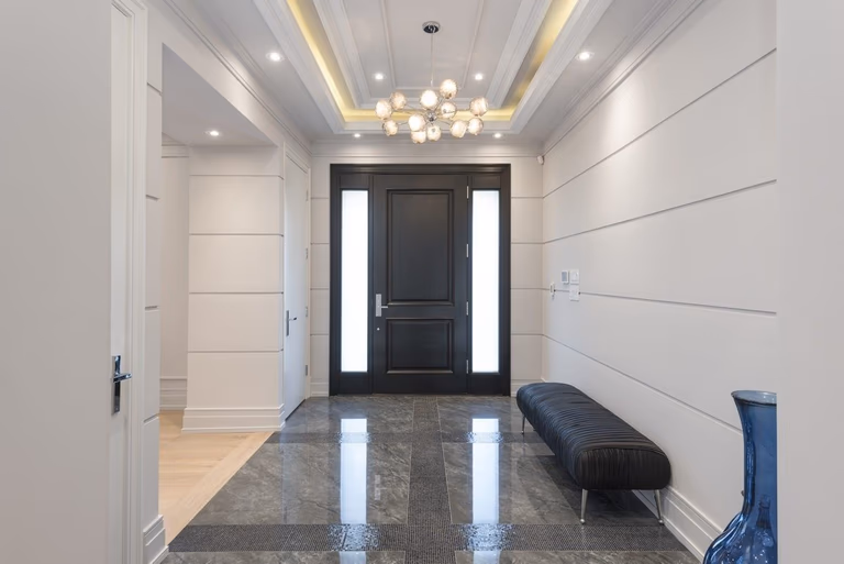 This Newmarket interior renovation features a modern luxury entrance design completed by a professional Toronto renovation company. The project includes custom wall paneling, elegant ceiling detailing with recessed lighting, polished stone flooring, and a contemporary chandelier to create a bright and welcoming foyer. The upgraded front entrance enhances both functionality and visual appeal, reflecting high-end craftsmanship and thoughtful interior planning for modern residential living in Newmarket and the GTA.