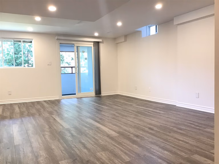 Bright and fully finished basement living space completed in this Richmond Hill basement renovation project. Featuring recessed pot lights, durable wood-look vinyl flooring, large windows, and walk-out access, this modern basement transformation creates a comfortable and functional extension of the home.