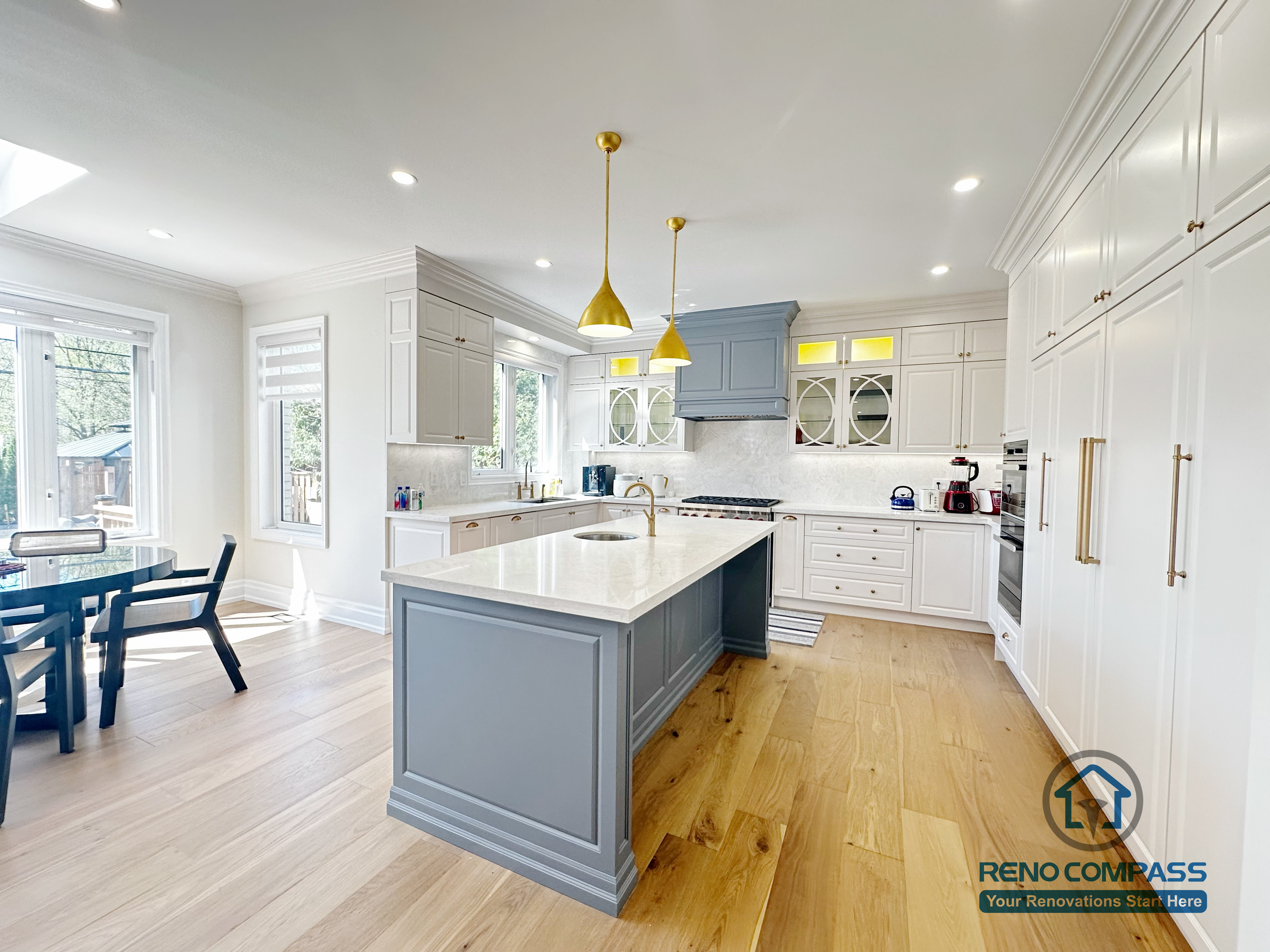 This North York kitchen renovation highlights a quartz waterfall island with an integrated sink, paired with warm brass pendant lighting and custom shaker cabinetry. The combination of functional workspace and layered lighting creates a bright, inviting kitchen designed for both daily use and entertaining, completed by Reno Compass.