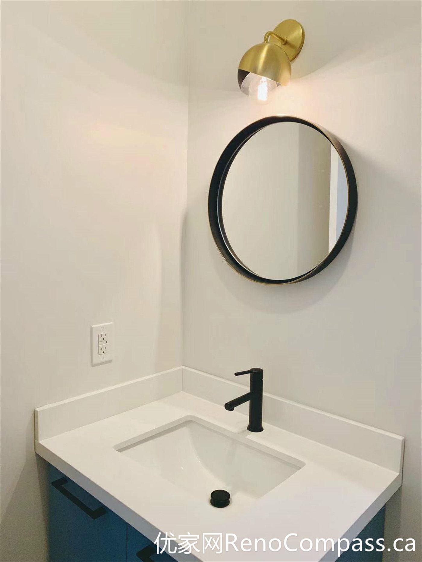 This Markham bathroom renovation features a compact vanity setup enhanced by a round mirror and a warm-toned wall sconce. The combination of soft lighting, matte black faucet, and clean white surfaces creates a cozy yet modern atmosphere, ideal for smaller bathroom spaces.