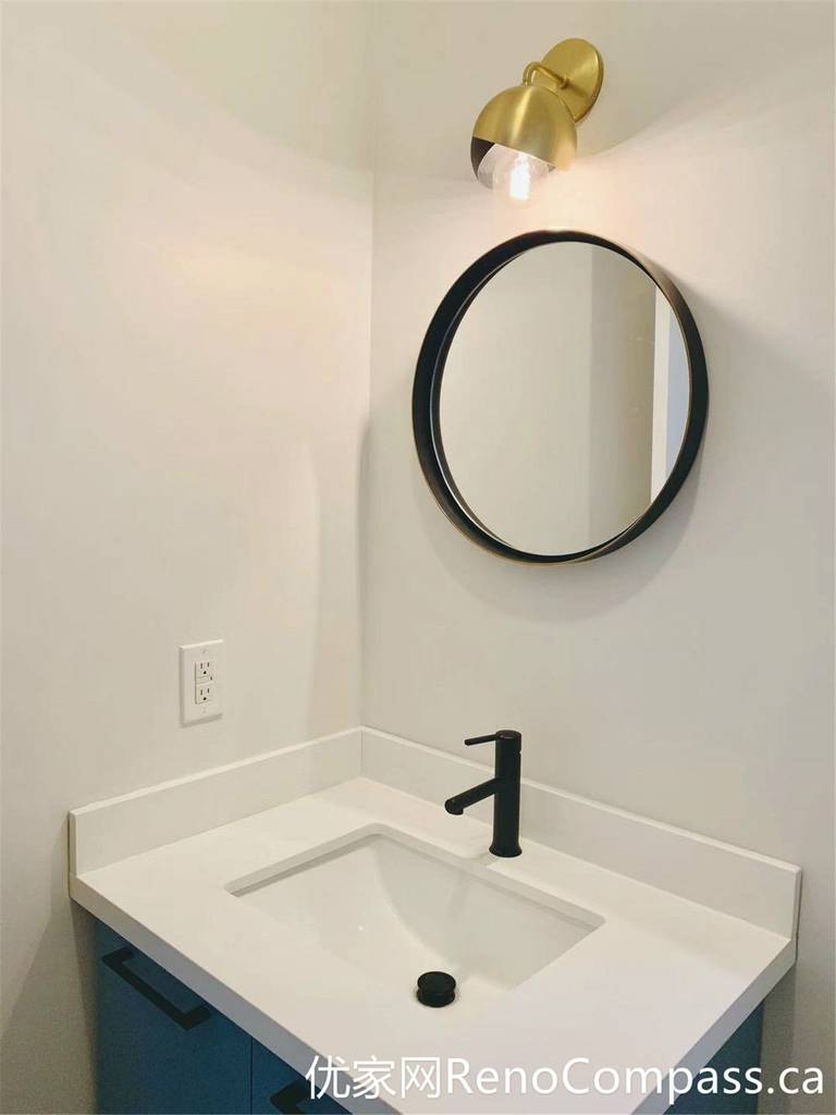 This Markham bathroom renovation features a compact vanity setup enhanced by a round mirror and a warm-toned wall sconce. The combination of soft lighting, matte black faucet, and clean white surfaces creates a cozy yet modern atmosphere, ideal for smaller bathroom spaces.
