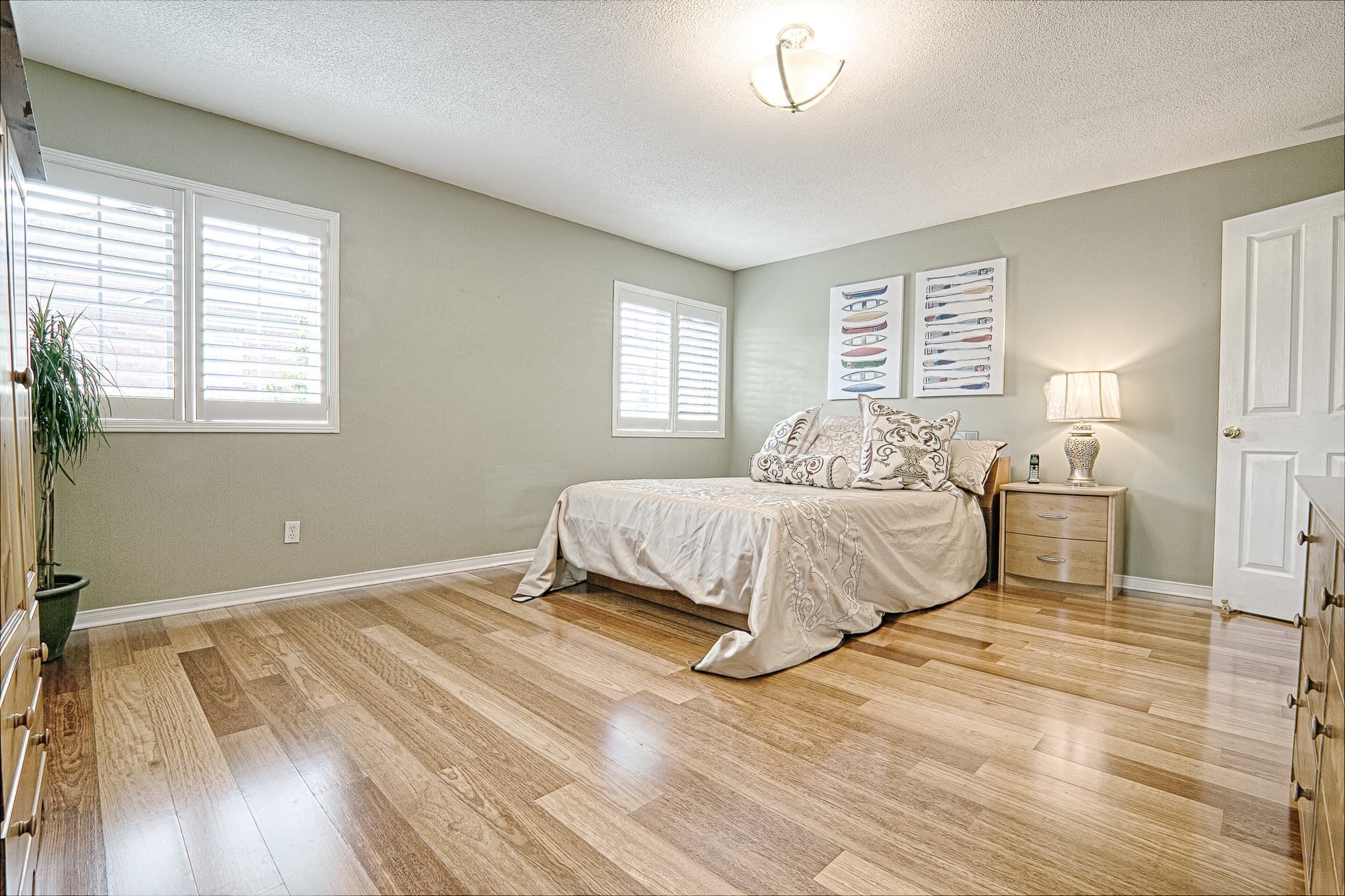 This warm minimalist bedroom interior features soft neutral wall tones, natural hardwood flooring, and clean-lined furniture that create a bright and inviting atmosphere. The spacious layout, modern dresser with framed mirror, and simple yet elegant bedding design reflect a balanced combination of comfort and functionality. Ideal inspiration for homeowners looking for cozy interior design and modern home styling ideas in Toronto and the GTA.
