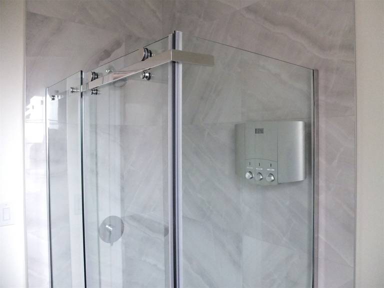 Modern bathroom renovation in a Scarborough home addition project featuring a frameless glass shower enclosure, marble-look wall tiles, and integrated shower system controls. The design enhances both elegance and functionality within the newly expanded residential space.