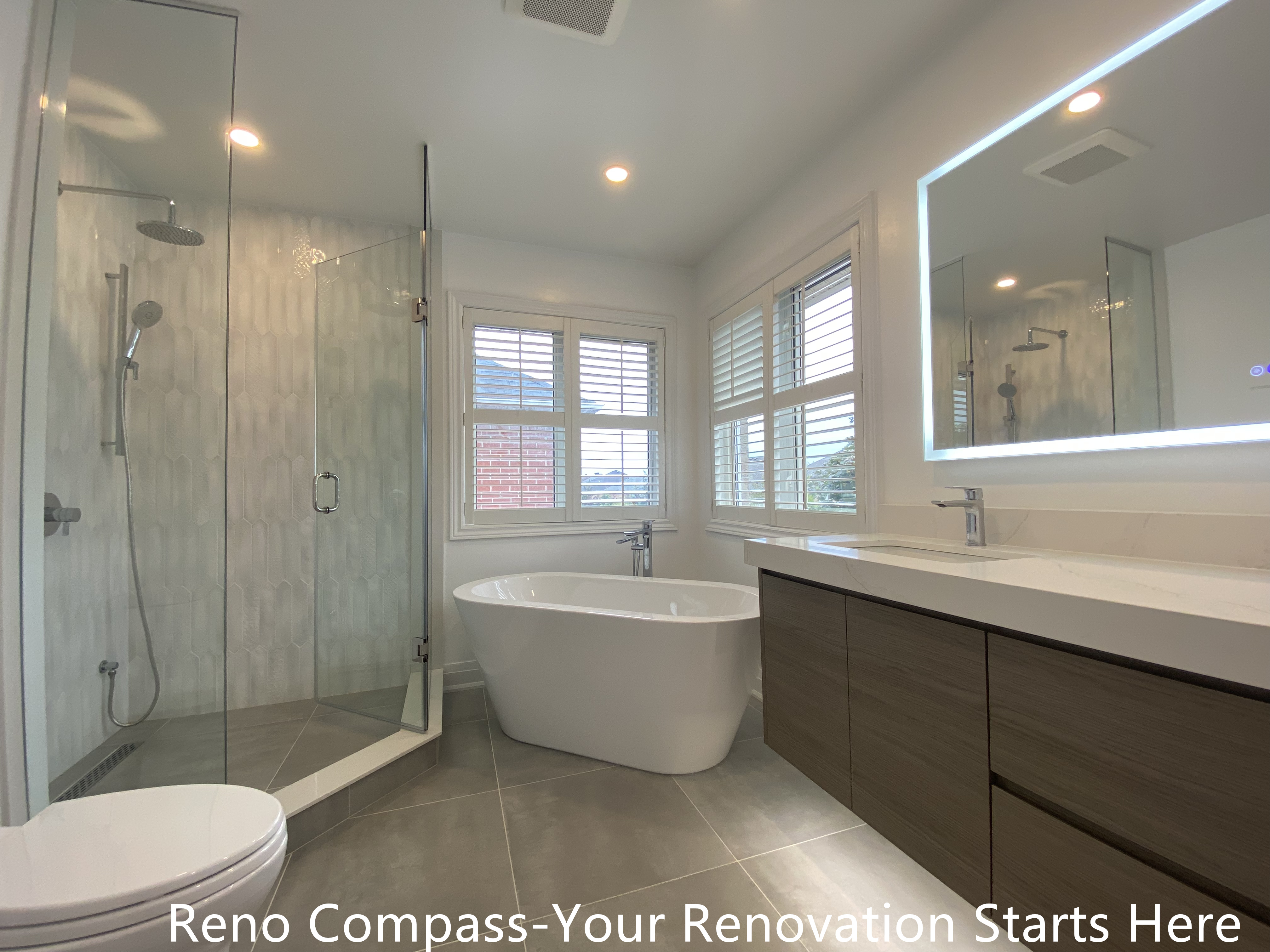Modern ensuite bathroom featured in an Oakville interior renovation, showcasing a freestanding bathtub, frameless glass shower, double sink vanity, and large LED mirror. The space is designed to maximize natural light, comfort, and functionality, delivering a refined bathroom upgrade by a professional Toronto renovation company.