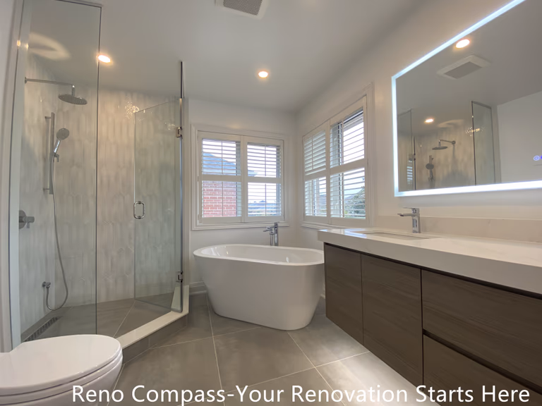 Modern ensuite bathroom featured in an Oakville interior renovation, showcasing a freestanding bathtub, frameless glass shower, double sink vanity, and large LED mirror. The space is designed to maximize natural light, comfort, and functionality, delivering a refined bathroom upgrade by a professional Toronto renovation company.