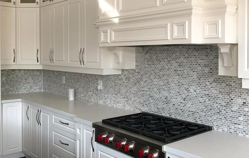 Close-up of a luxury Markham kitchen renovation featuring custom white cabinetry, detailed crown molding range hood, mosaic tile backsplash, and professional gas cooktop. Quartz countertops and modern hardware enhance both functionality and elegance. This refined kitchen design was completed by a trusted Toronto renovation company, combining craftsmanship with timeless style for upscale residential living.