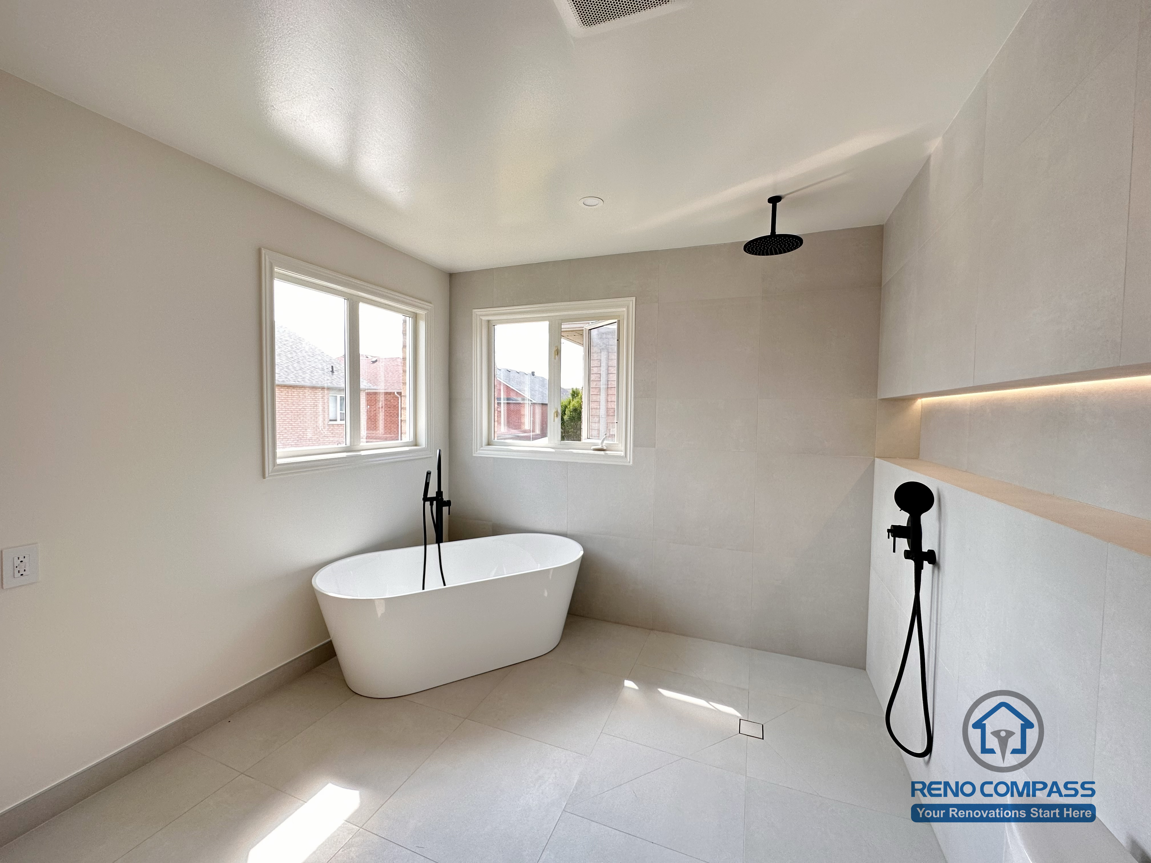 Modern bathroom renovation in Markham featuring a freestanding bathtub, walk-in shower, and wall-mounted matte black fixtures. Large-format tiles, soft natural light, and a minimalist layout create a calm, spa-like bathroom designed for comfort and everyday use.