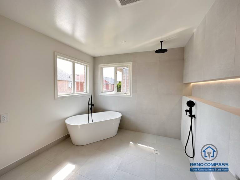 Modern bathroom renovation in Markham featuring a freestanding bathtub, walk-in shower, and wall-mounted matte black fixtures. Large-format tiles, soft natural light, and a minimalist layout create a calm, spa-like bathroom designed for comfort and everyday use.