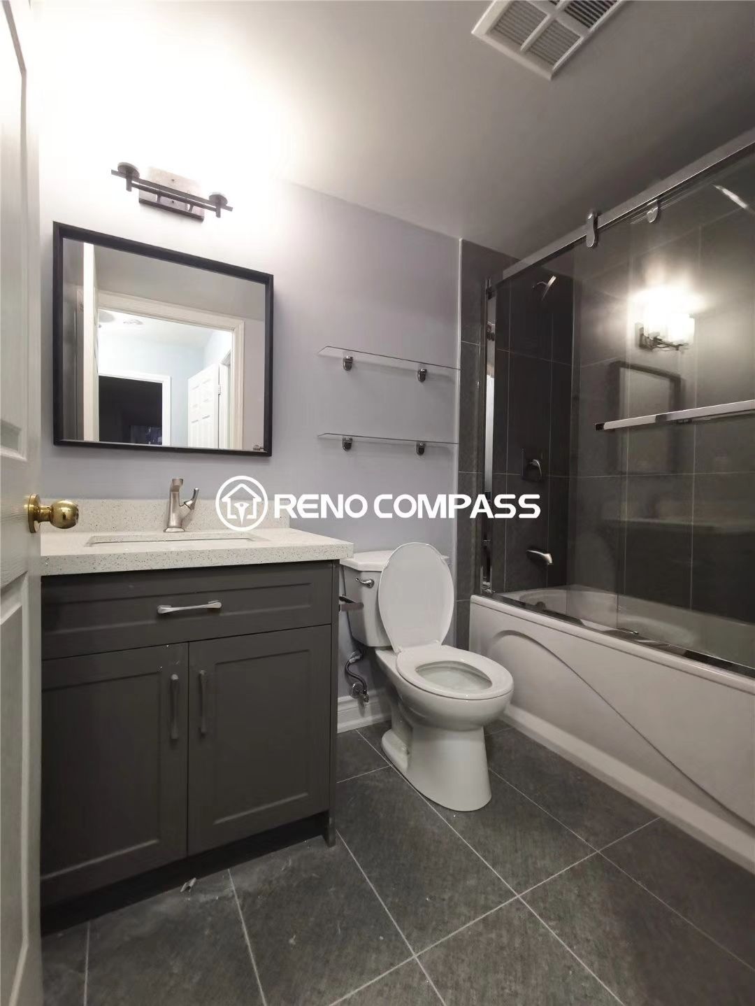 This Richmond Hill condo bathroom renovation features a modern vanity installation with new cabinetry, updated countertop, stylish mirror lighting, and a refreshed bathtub with sliding glass shower doors. Grey tile flooring and clean wall finishes create a contemporary and functional bathroom space suited for condominium living. The renovation focuses on maximizing space efficiency while improving comfort and aesthetics. Completed by Reno Compass, a trusted Toronto renovation company, this project highlights high-quality condo bathroom remodeling designed to enhance daily living and increase property value.