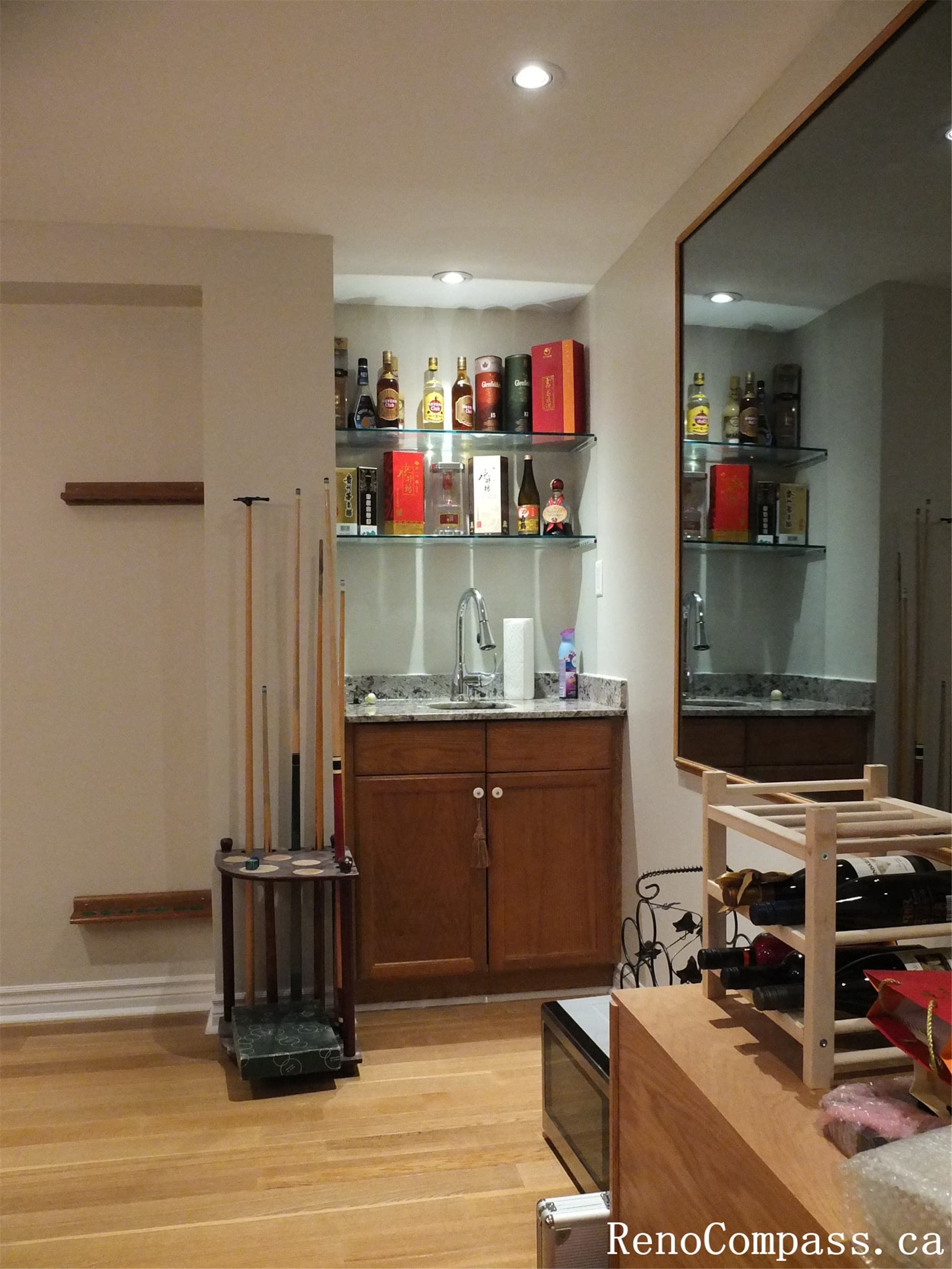 This custom basement bar area is part of a North York interior renovation, designed to integrate storage, display, and everyday functionality within a compact footprint. The renovation features built-in wood cabinetry, open glass shelving for liquor display, and a stone countertop with an integrated sink. Recessed lighting enhances visibility while maintaining a warm, residential atmosphere. Completed by a Toronto renovation company, this basement bar renovation focuses on clean lines, durable finishes, and seamless integration with the surrounding entertainment space.