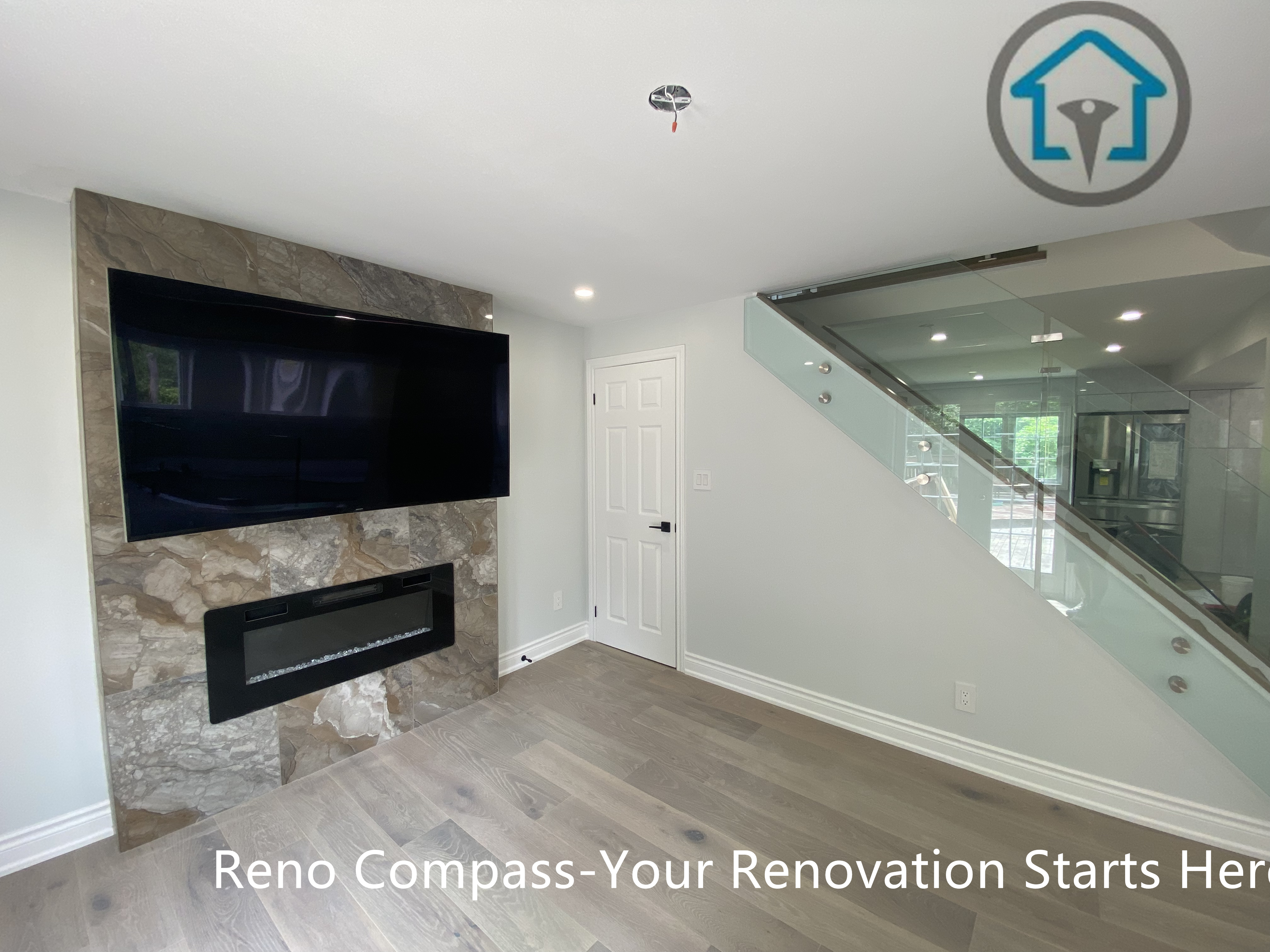 This Stouffville living space showcases a modern glass staircase paired with wide-plank flooring and a stone feature wall with a built-in fireplace. The open layout enhances visual flow while maintaining a clean, contemporary aesthetic.