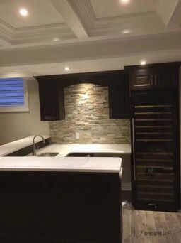 Modern kitchen renovation in Scarborough featuring dark custom cabinetry, white stone countertop, textured backsplash wall, and elegant pendant lighting that creates a warm and contemporary interior atmosphere.