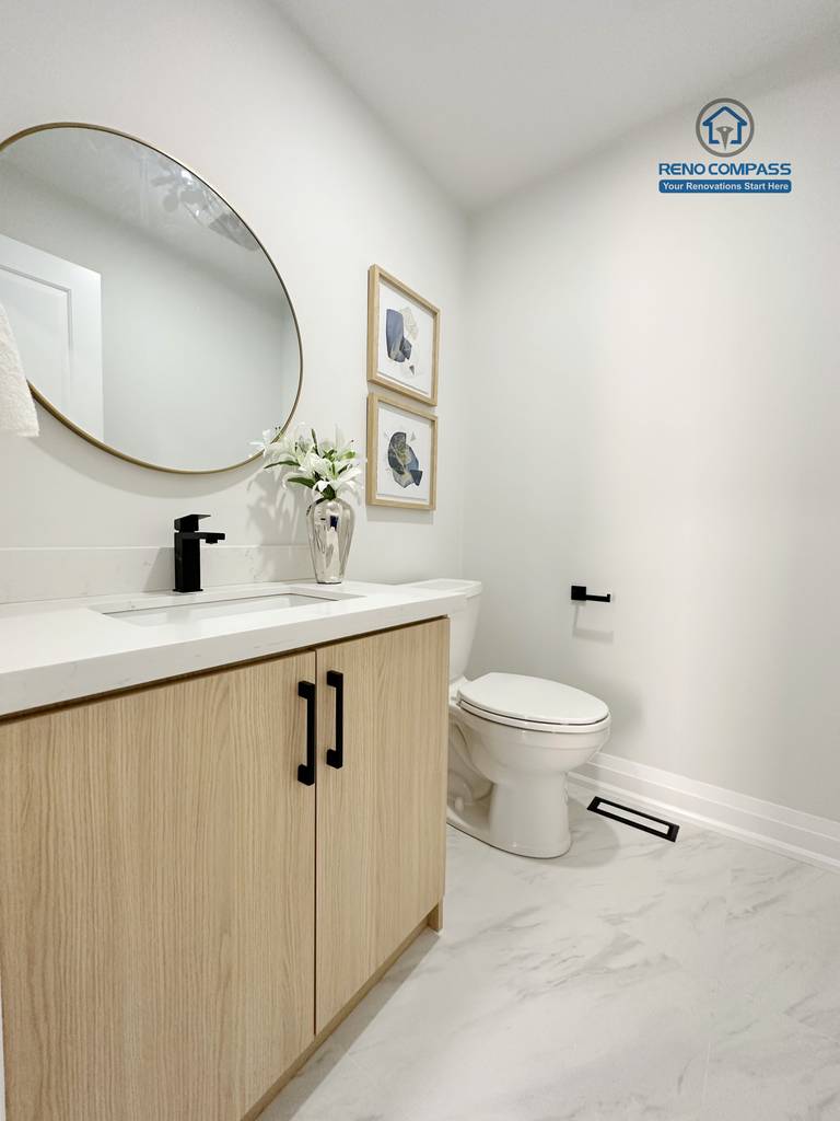 This Richmond Hill interior renovation showcases a modern bathroom vanity with natural wood cabinetry, quartz countertop, and a round mirror with black fixtures. The clean layout and neutral tones create a bright and functional powder room. Completed by a Toronto renovation company, the space balances practicality with contemporary style.