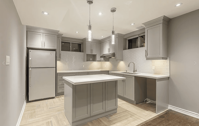 This Toronto basement renovation features a modern custom kitchen with grey shaker cabinets, quartz countertops, a center island, and upgraded lighting. Designed for functionality and style, this basement kitchen includes full cabinetry installation, backsplash tiling, stainless steel appliances, and optimized layout for comfortable living. Completed by a professional Toronto renovation company specializing in basement finishing and interior upgrades.