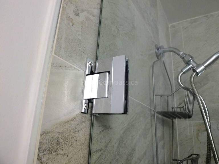 This image captures a close-up of a frameless glass shower door hinge installed during a North York interior renovation project. The solid chrome hinge is precisely mounted into tiled walls, ensuring smooth door operation, long-term durability, and a clean, minimalist appearance. Combined with marble-look wall tiles and modern shower fixtures, the detail reflects careful hardware selection and professional installation by a trusted Toronto renovation company.