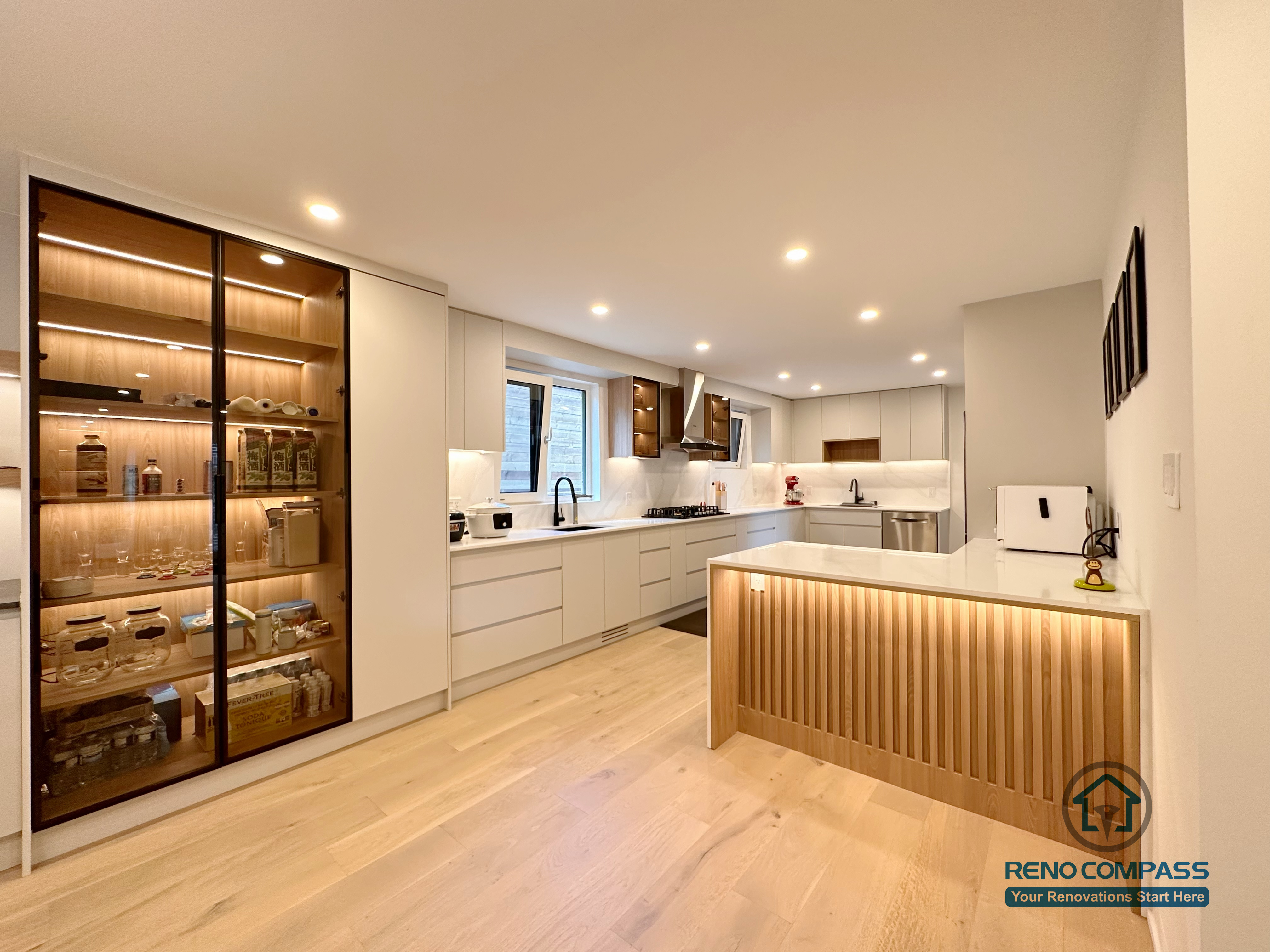 A modern open-concept kitchen renovation in Toronto featuring full custom cabinetry, integrated LED lighting, a minimalist island design, and warm wood accents. This whole-house custom cabinet project combines functionality and clean aesthetics, showcasing high-end craftsmanship by a professional Toronto renovation company.