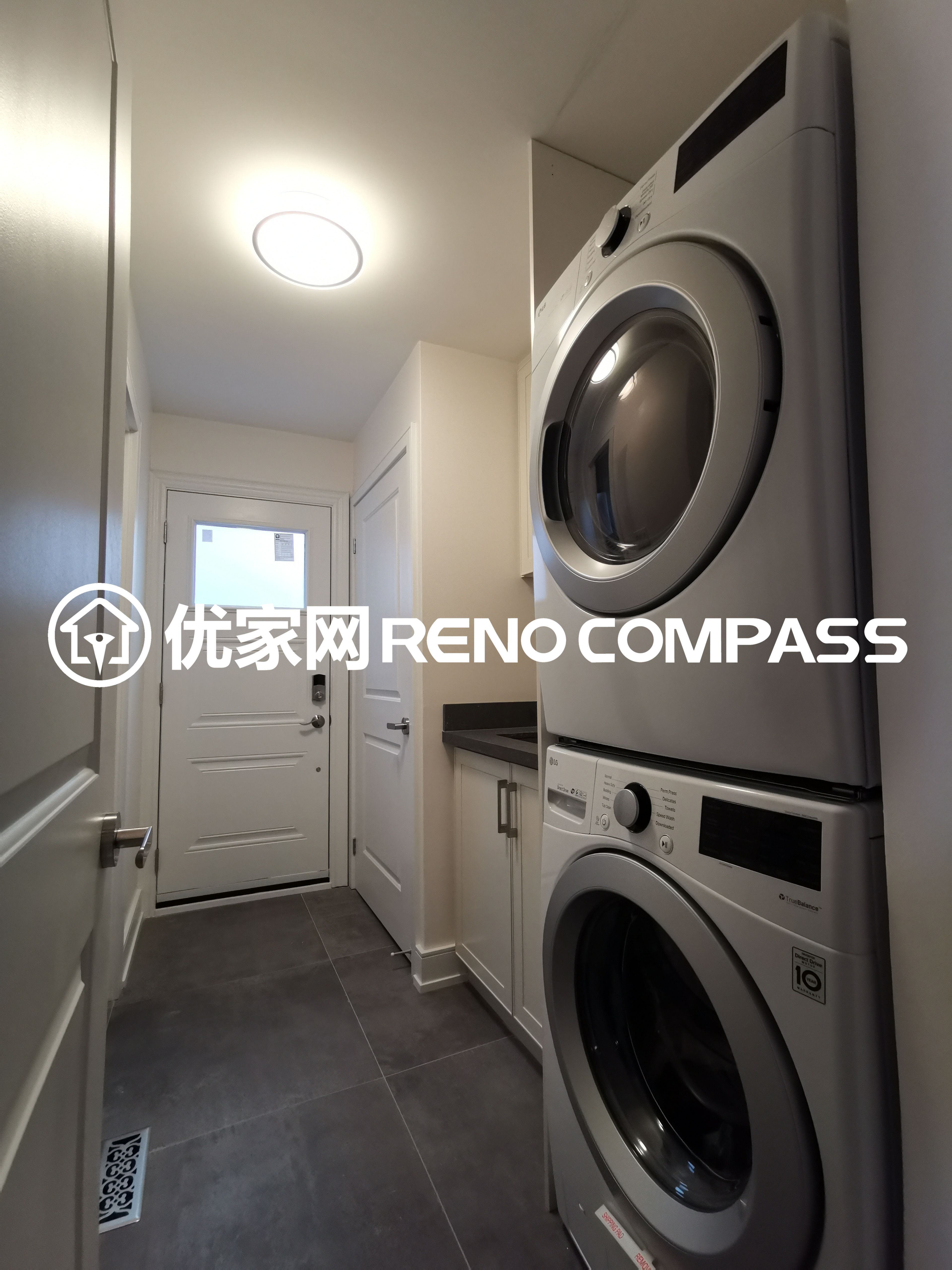This image features a compact laundry room completed as part of a North York interior renovation project. The space includes a stacked washer and dryer configuration to maximize vertical space, paired with custom cabinetry and a durable tiled floor for everyday practicality. Recessed ceiling lighting provides bright and even illumination, while the streamlined layout allows smooth access to the exterior door. The design reflects efficient space planning, functional storage solutions, and quality workmanship tailored for modern Toronto homes.