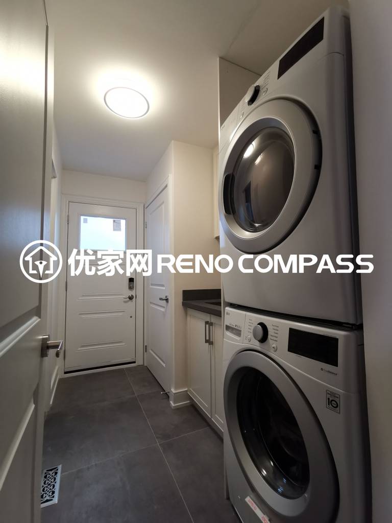 This image features a compact laundry room completed as part of a North York interior renovation project. The space includes a stacked washer and dryer configuration to maximize vertical space, paired with custom cabinetry and a durable tiled floor for everyday practicality. Recessed ceiling lighting provides bright and even illumination, while the streamlined layout allows smooth access to the exterior door. The design reflects efficient space planning, functional storage solutions, and quality workmanship tailored for modern Toronto homes.