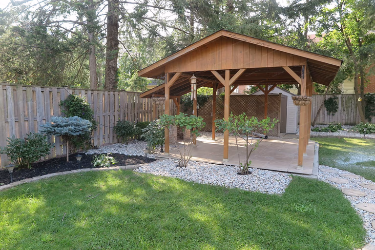 This image showcases a North York landscaping renovation featuring a custom-built wooden pavilion integrated with surrounding lawn, planting beds, and decorative stone borders. The structure provides shaded outdoor living space while maintaining visual balance and natural flow within the backyard layout. Completed by a Toronto Renovation Company specializing in landscape renovation and outdoor structure construction.