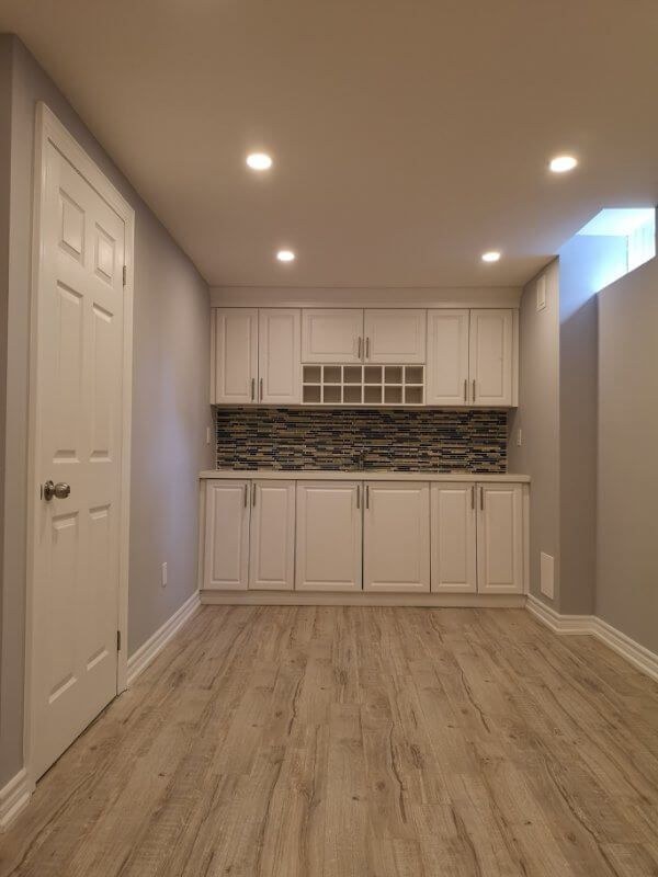This Markham finished basement renovation features a modern kitchenette with custom white cabinetry, mosaic backsplash, and durable flooring in a bright open layout. Completed by a professional Toronto renovation company, the project creates a functional and stylish basement living space ideal for rental potential, entertainment, or extended family use.