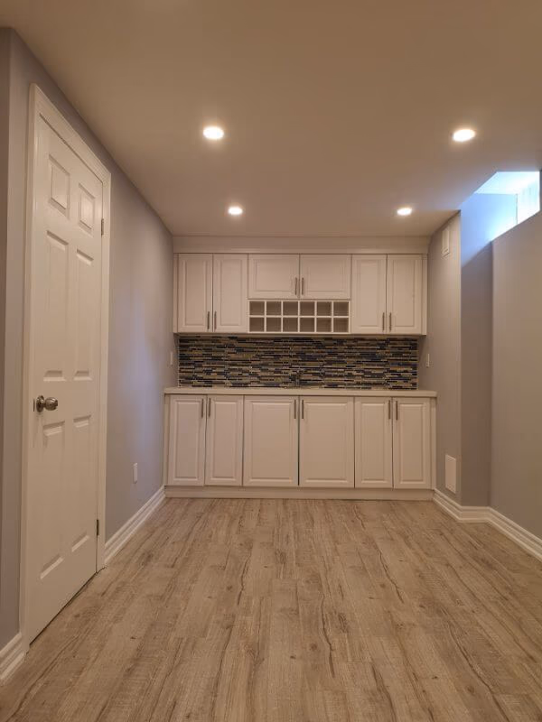 This Markham finished basement renovation features a modern kitchenette with custom white cabinetry, mosaic backsplash, and durable flooring in a bright open layout. Completed by a professional Toronto renovation company, the project creates a functional and stylish basement living space ideal for rental potential, entertainment, or extended family use.