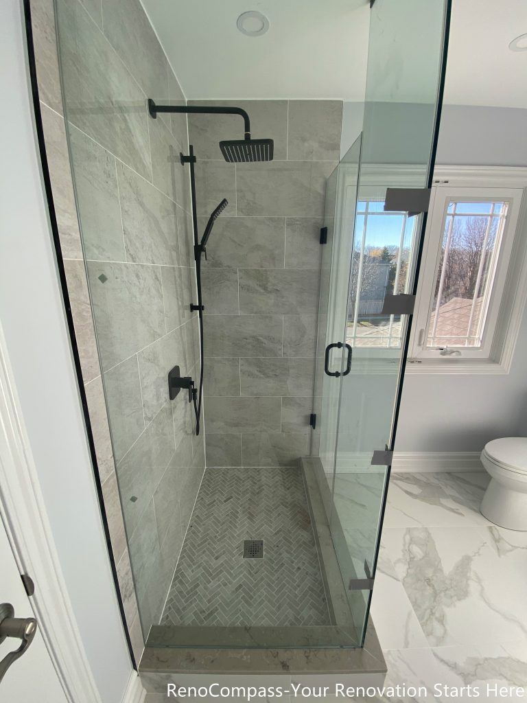This Thornhill bathroom renovation features a walk-in glass shower with a herringbone-patterned tile base and a centered floor drain for efficient water management. Large-format gray wall tiles create a clean and structured appearance, while the frameless glass enclosure maintains visual openness and brightness. Matte black fixtures complement the neutral tones, resulting in a practical, well-proportioned shower design focused on durability, comfort, and everyday functionality.