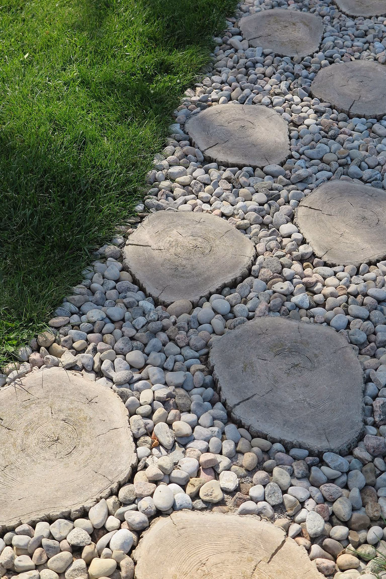 Custom garden pathway installation in North York featuring natural stepping stones set over decorative river rocks and lush green lawn. This professionally designed landscaping detail by Reno Compass enhances backyard functionality while creating a serene and modern outdoor walking path.