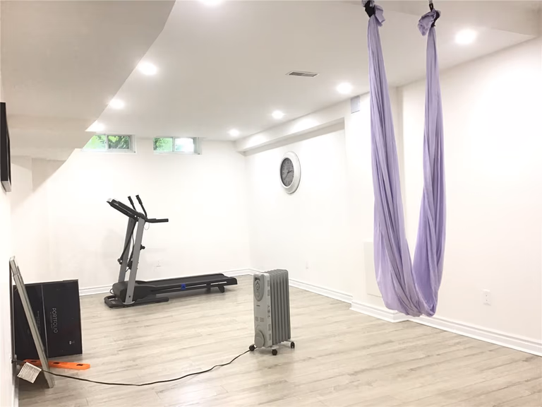 This Aurora basement renovation features a dedicated home gym and wellness area with an open and minimalist layout. The space includes a treadmill, aerial yoga setup, and wide plank flooring, enhanced by recessed ceiling lights for a bright and comfortable workout environment.