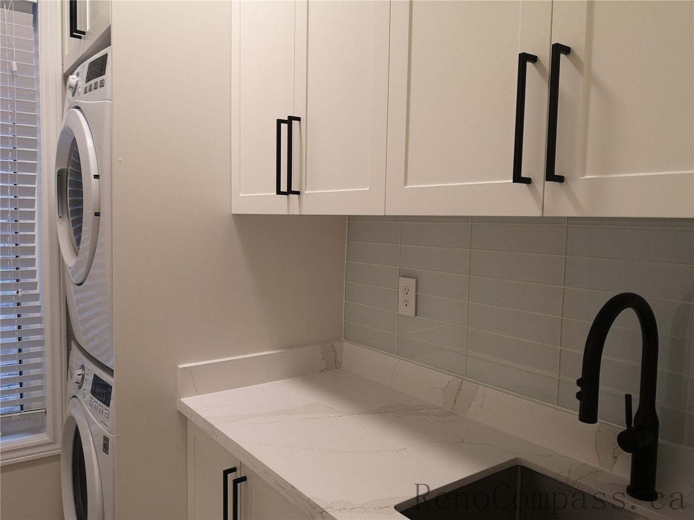 This Aurora interior renovation features a modern laundry room with custom white shaker cabinets, quartz countertop, and integrated utility sink with matte black faucet. The stacked washer and dryer design maximizes space while maintaining a clean and functional layout. Completed by a professional Toronto renovation company focused on efficient storage solutions, modern finishes, and high-quality craftsmanship for everyday living.