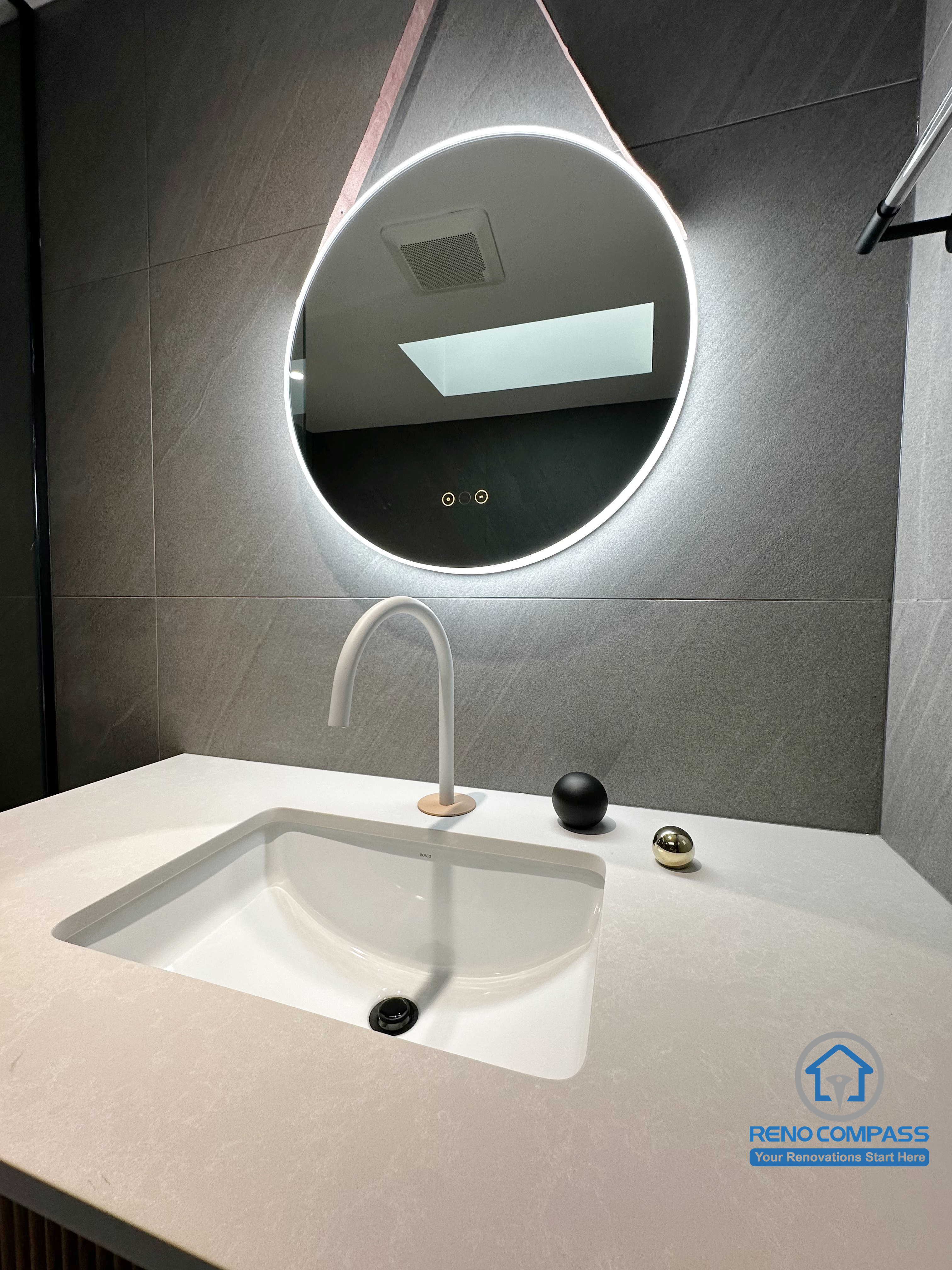 This detail shot highlights the bathroom vanity and backlit mirror from a Richmond Hill renovation. The integrated sink, sculptural modern faucet, and soft LED lighting create a clean, contemporary look, while the neutral grey tile backdrop enhances depth and visual balance. Designed and completed by Reno Compass, this space reflects a refined modern bathroom aesthetic within the Greater Toronto Area.