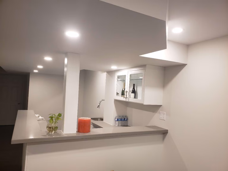 This Markham basement renovation features a custom-built bar and countertop area designed to enhance both functionality and style. The space includes modern white cabinetry, a built-in sink, upper storage cabinets, and a spacious serving counter suitable for entertaining and daily use. Recessed pot lights provide bright, even lighting, creating a warm and inviting atmosphere throughout the basement. Neutral finishes and durable materials ensure long-term practicality and easy maintenance. This professionally completed basement bar upgrade reflects quality craftsmanship and thoughtful space planning in a modern Markham basement renovation.