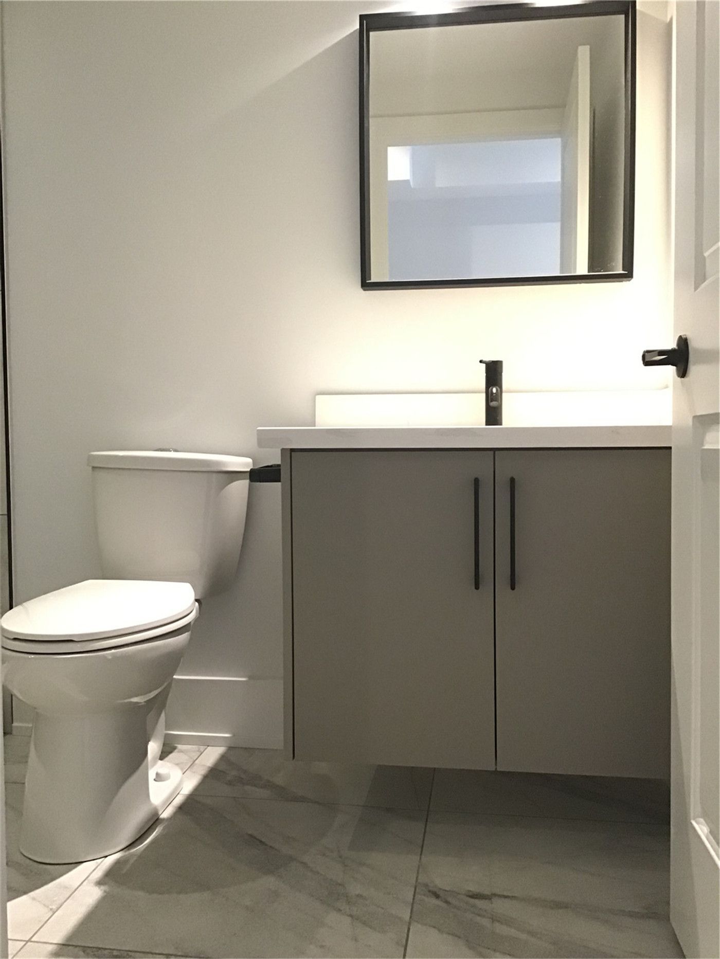 This Markham full home renovation features a compact and modern powder room with a sleek vanity, clean-lined mirror, and durable tile flooring. The neutral color palette and matte black fixtures create a simple yet elegant space, maximizing functionality in a smaller layout. Completed by a trusted Toronto Renovation Company, this design reflects efficient use of space with contemporary style.