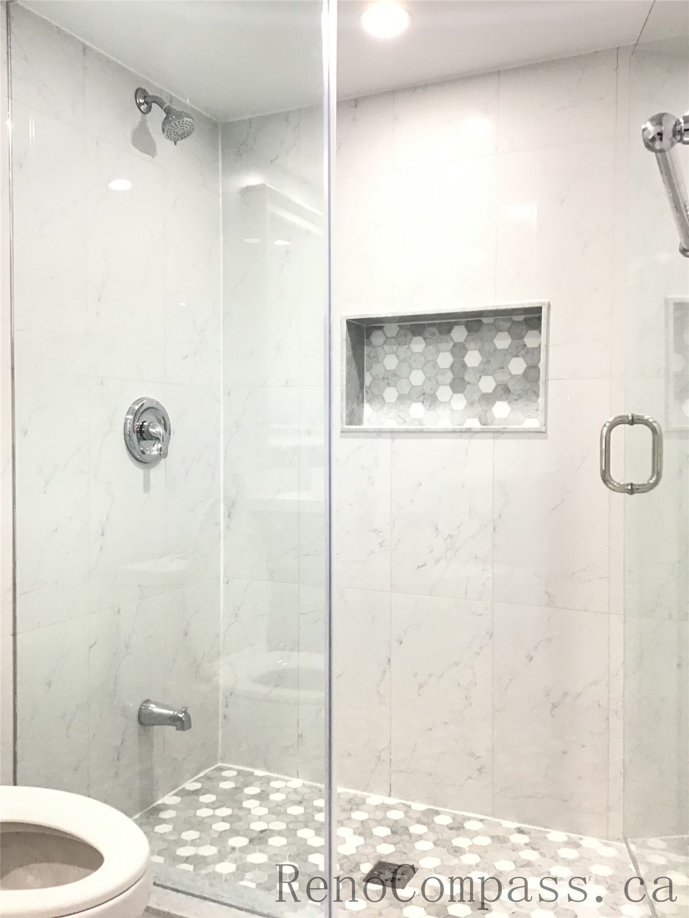 Modern basement bathroom renovation in Richmond Hill featuring a frameless glass shower enclosure, marble-look wall tiles, hexagon mosaic shower floor, and built-in niche shelving. Finished with chrome fixtures and recessed lighting, this elegant shower upgrade adds both luxury and practicality to the basement renovation completed by a professional Toronto Renovation Company.