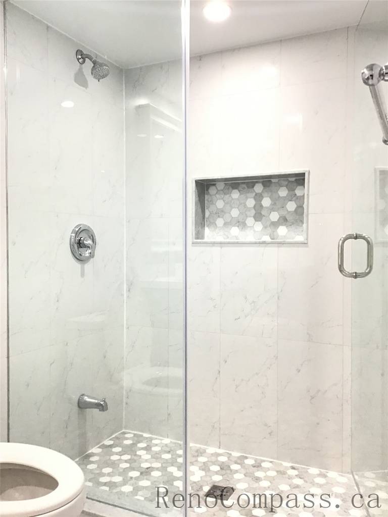 Modern basement bathroom renovation in Richmond Hill featuring a frameless glass shower enclosure, marble-look wall tiles, hexagon mosaic shower floor, and built-in niche shelving. Finished with chrome fixtures and recessed lighting, this elegant shower upgrade adds both luxury and practicality to the basement renovation completed by a professional Toronto Renovation Company.